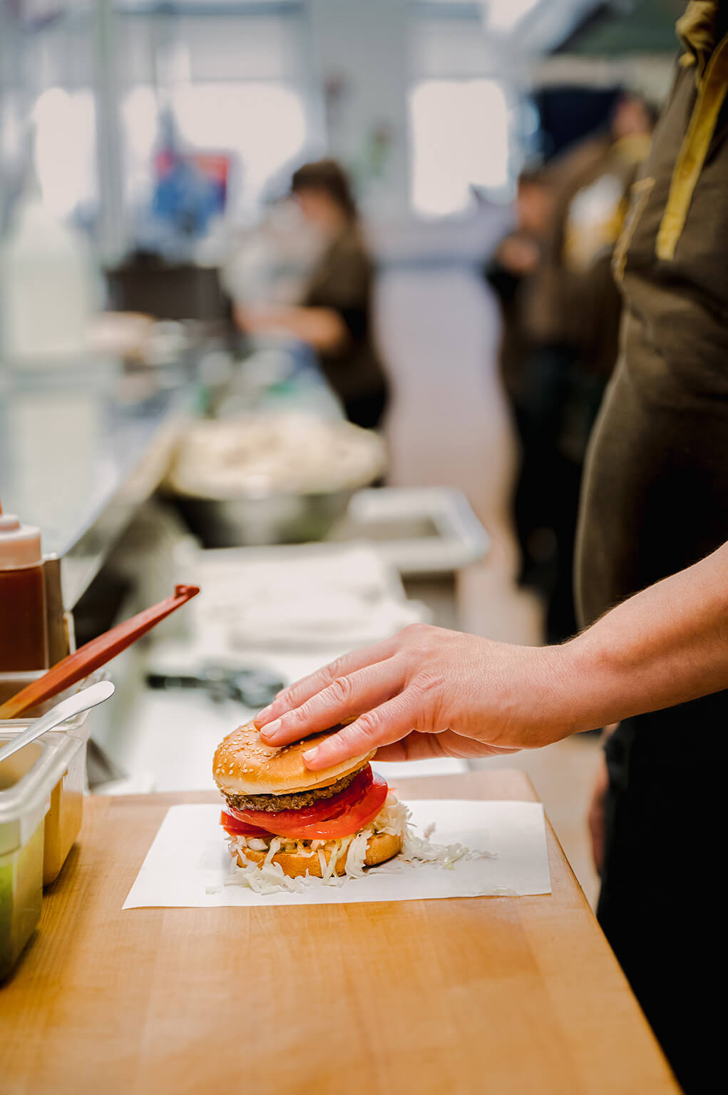 A hand making a burger with meat, lettuce in a fast-food restaurant kitchen