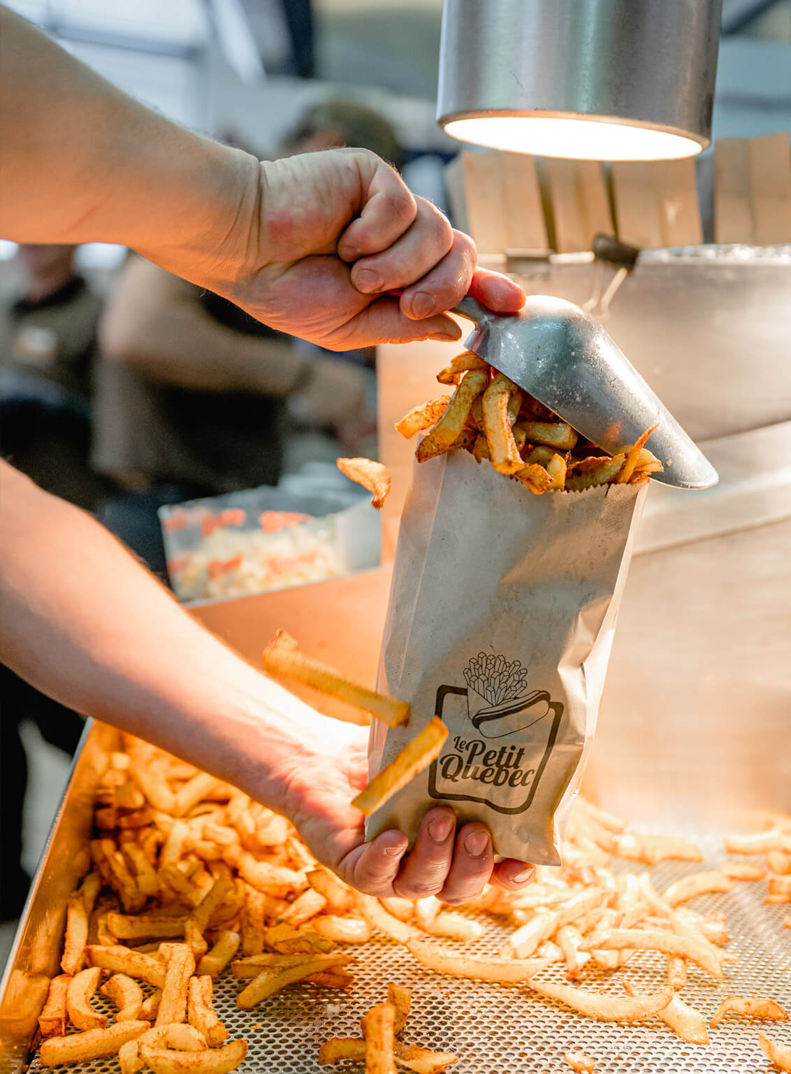 Hand putting fries in a Le Petit Québec paper bag in a fast-food restaurant